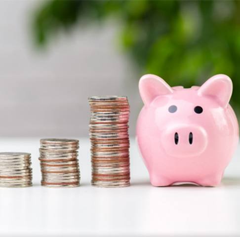 Stacks of coins next to a piggy bank on a white counter