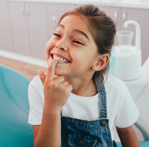 Smiling girl pointing to her teeth after dye-free children’s dentistry in Jeffersonville 