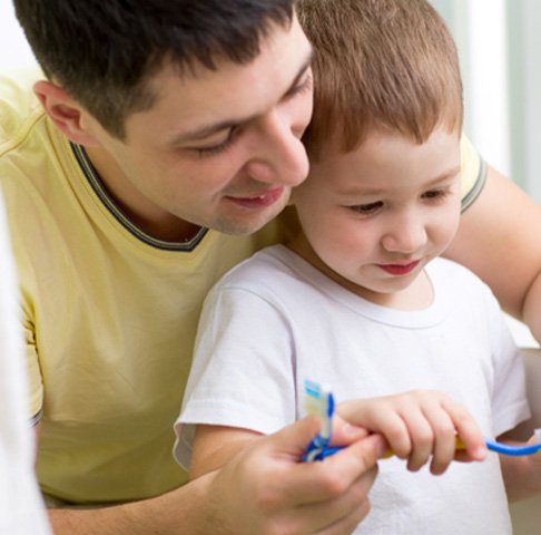 Father teaching son to put dye-free toothpaste in Jeffersonville on toothbrush 
