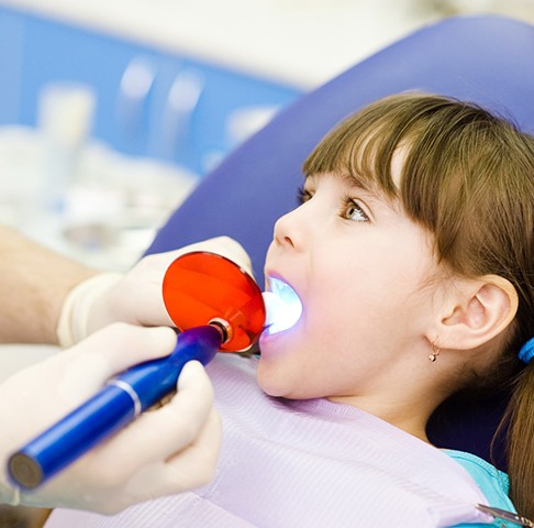 Young girl sitting in a dental chair having her kid’s filling sealed