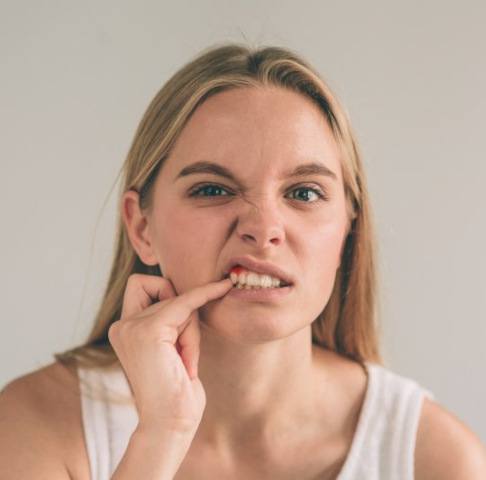 Blonde woman poking at her sensitive gums with a worried expression